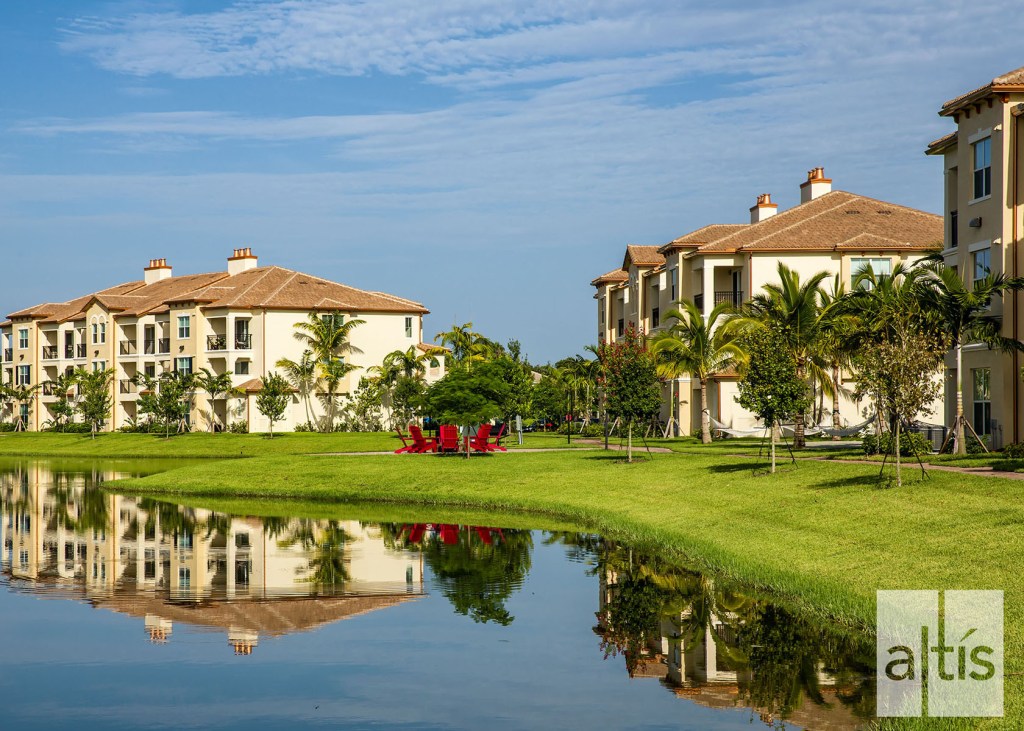 Mature palm trees and a lake with fire pit add visual interest to the flat Florida topography at Altis at Sheridan Village.