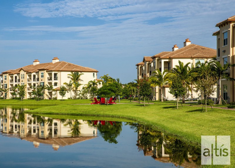 Mature palm trees and a lake with fire pit add visual interest to the flat Florida topography at Altis at Sheridan Village.